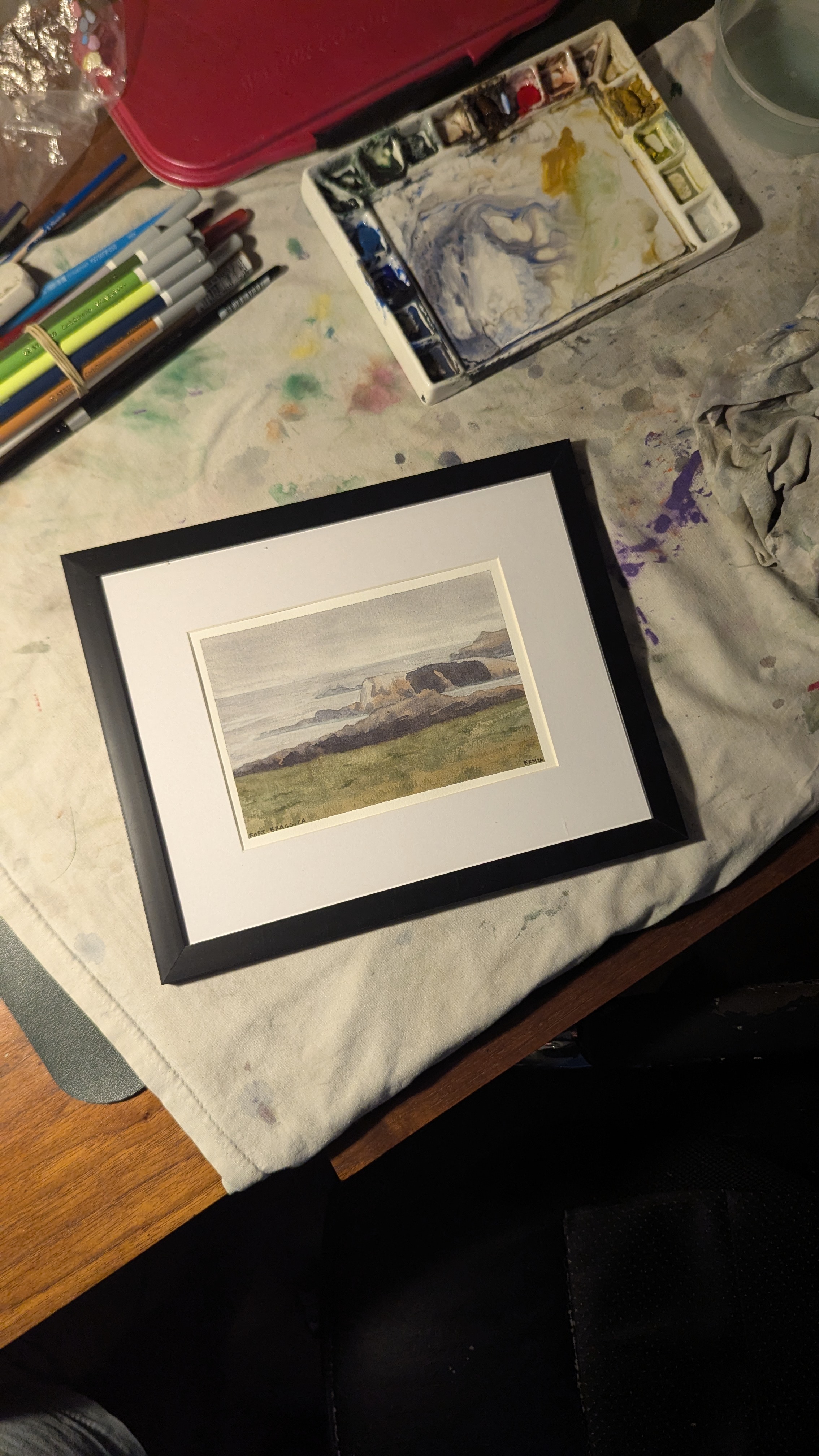 Watercolor painting of the beach at Fort Bragg, CA sitting on an artist's desk.